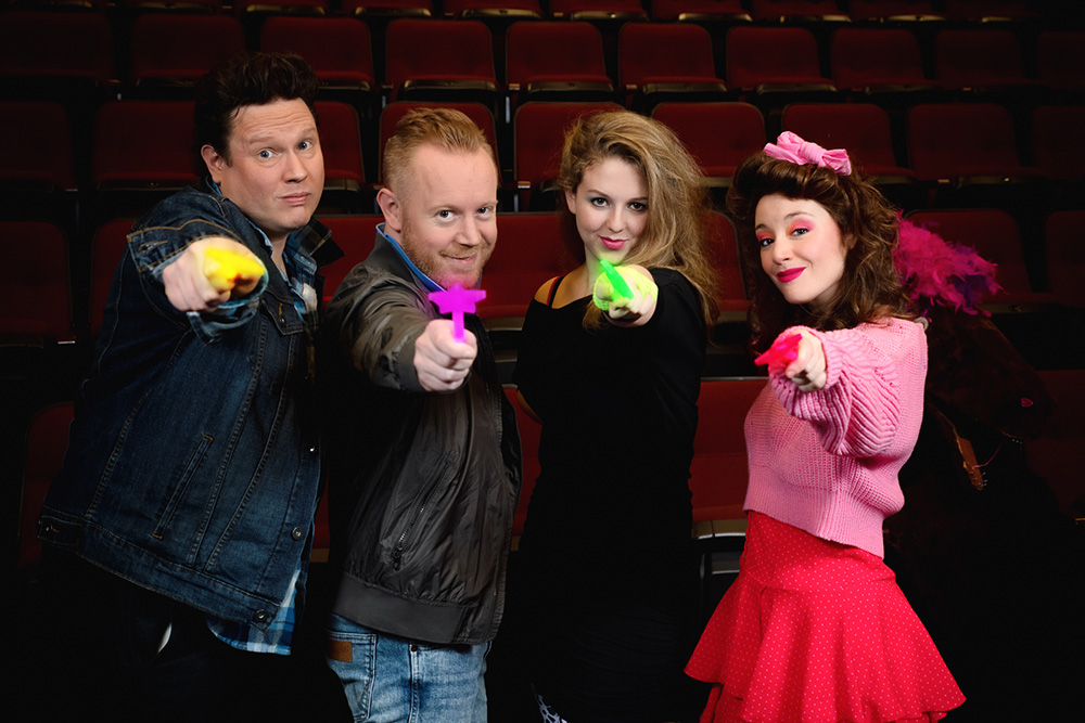 Photo of the cast of Seal Slippers in 80s costumes, holding magic wands at the camera.